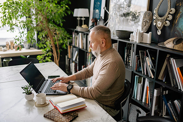 A man working on a laptop at a desk in his home library